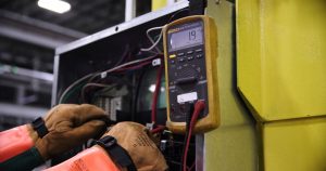 Electrician using a multimeter to fix industrial control panel wiring in Montreal
